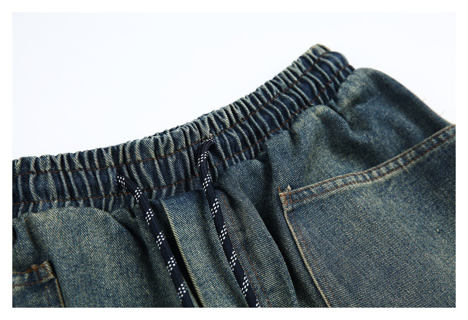 Close-up of the gathered elastic waistband, drawstrings, and pocket seam on denim shorts.