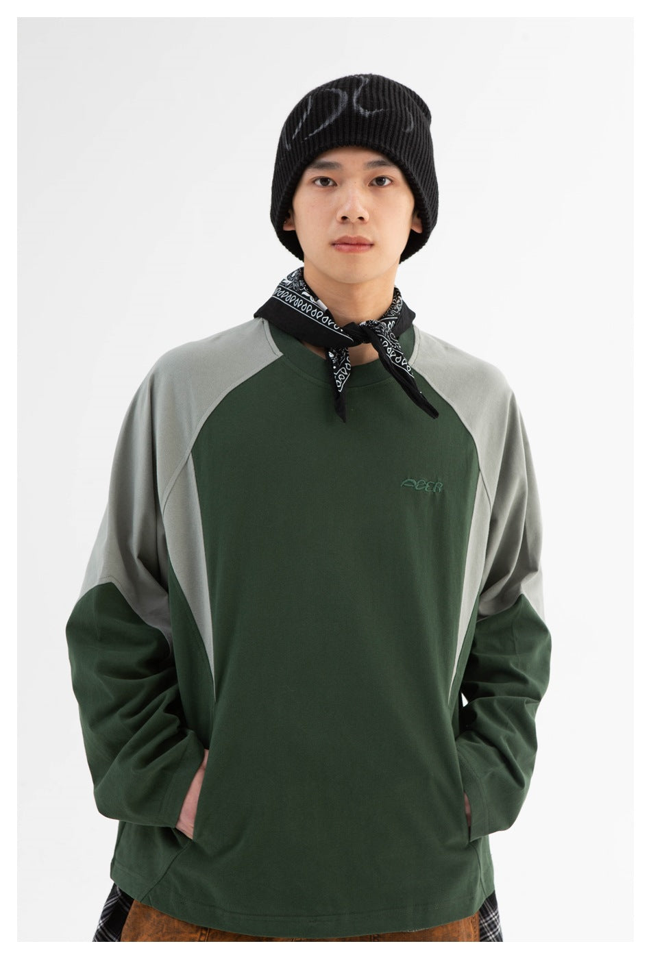 Model wearing a dark green raglan sweatshirt with light gray shoulder panels, a black beanie, and a patterned neck scarf.
