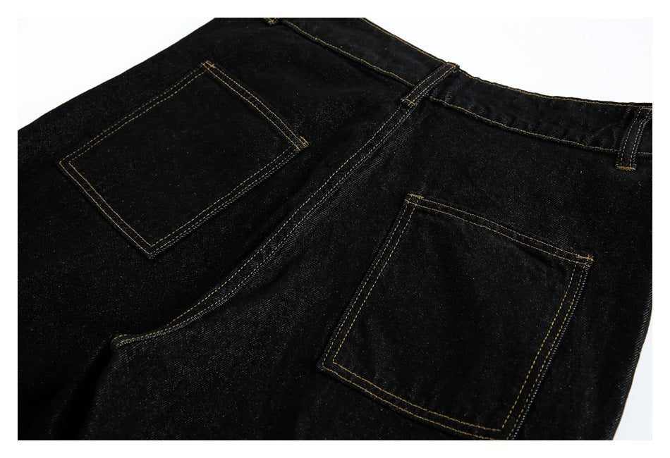 Cropped rear view of black jeans showing two square back pockets and golden contrast stitching.