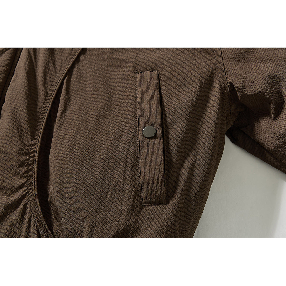Close-up of a dark brown jacket's vertical snap-tab pocket and textured fabric.