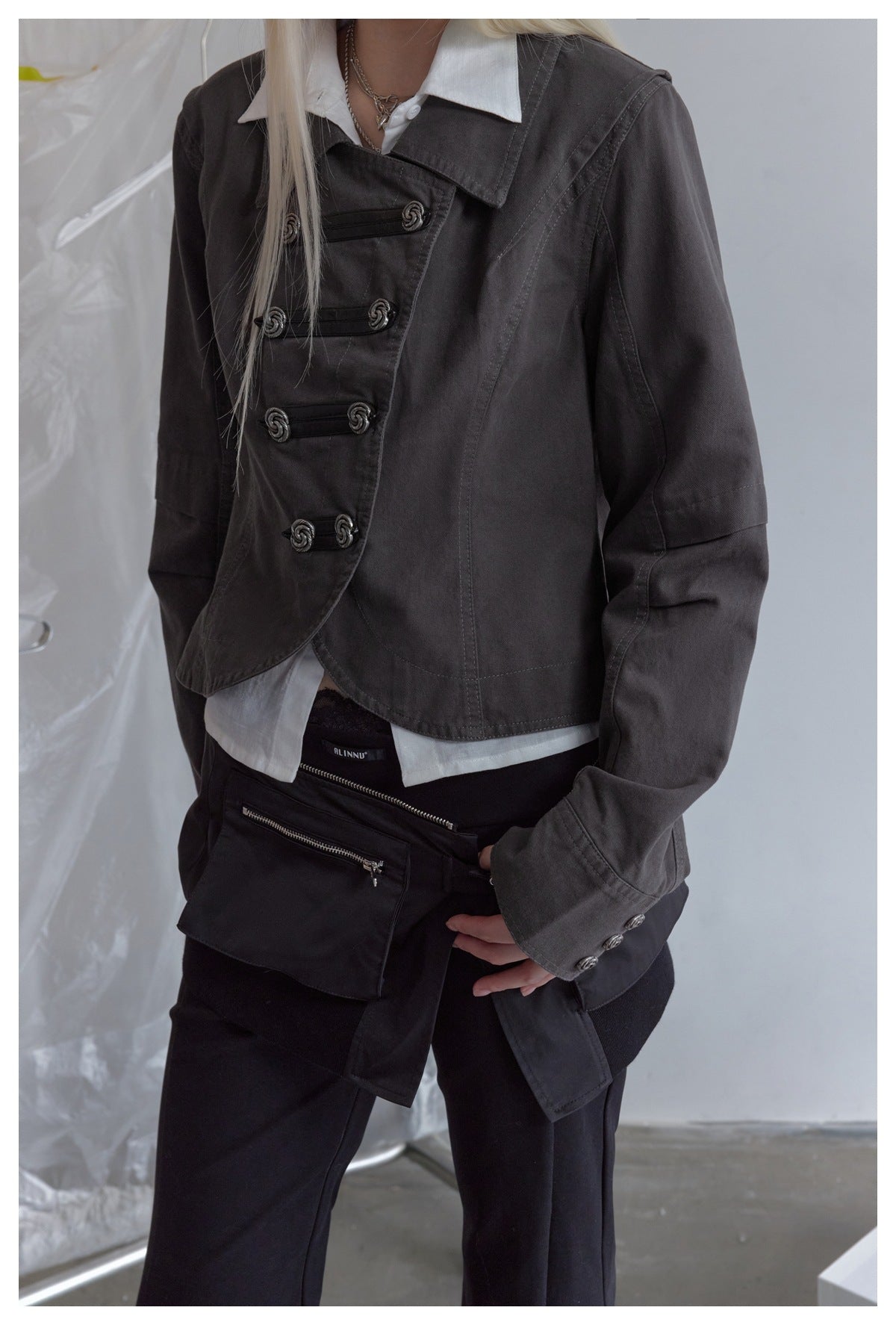 Close view of a model wearing a charcoal jacket with an asymmetrical front, silver-toned toggles, and a wide collar.