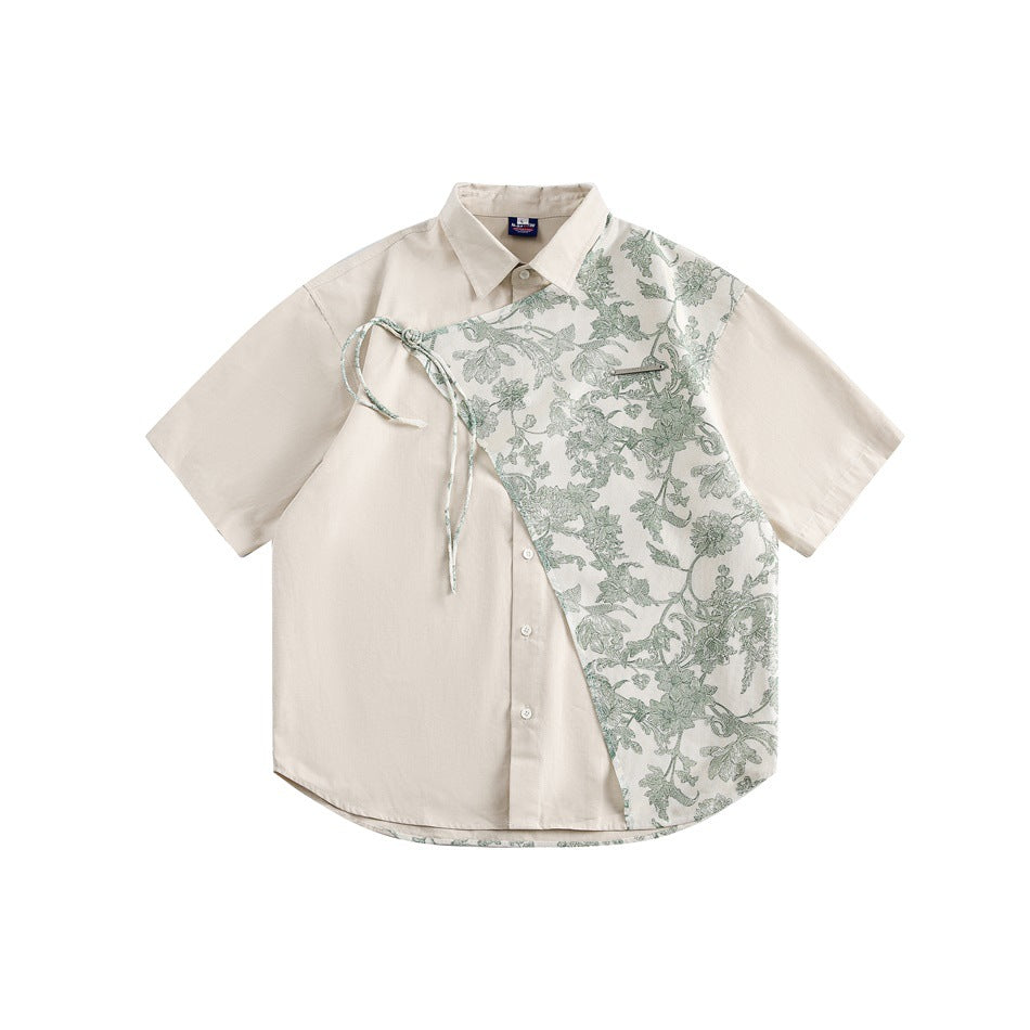 Beige short-sleeve button shirt with green floral diagonal overlay panel, tie cord and metal bar accent, flat lay