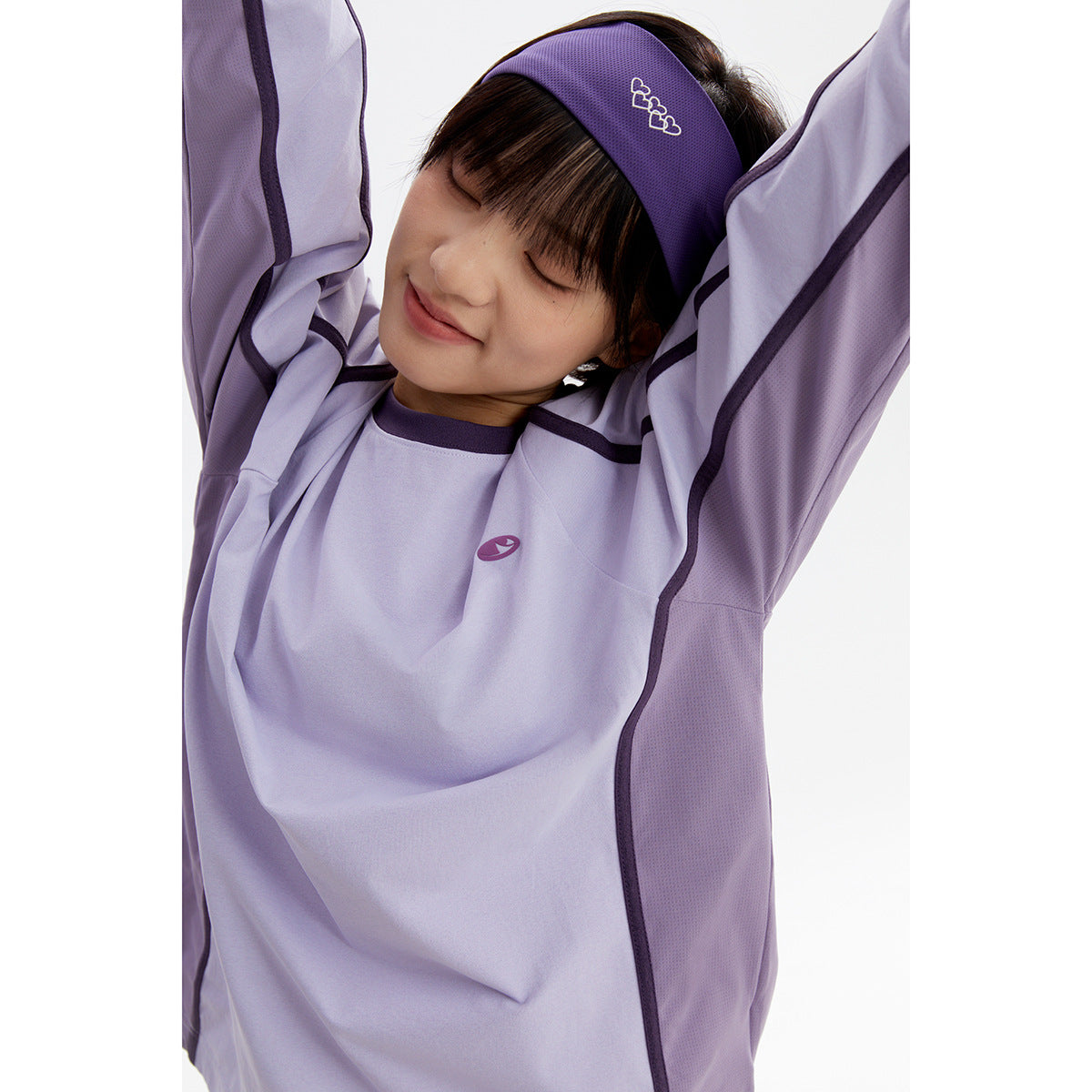 Close-up of a model wearing a pale lavender long-sleeve top with dark purple trim and a matching headband.