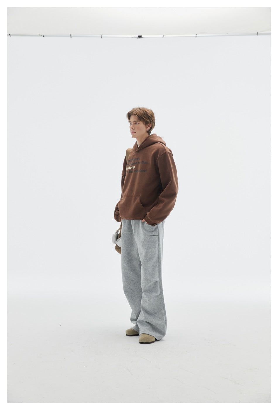 Model in a brown text-print hoodie and loose gray pants, shown at a slight side angle.