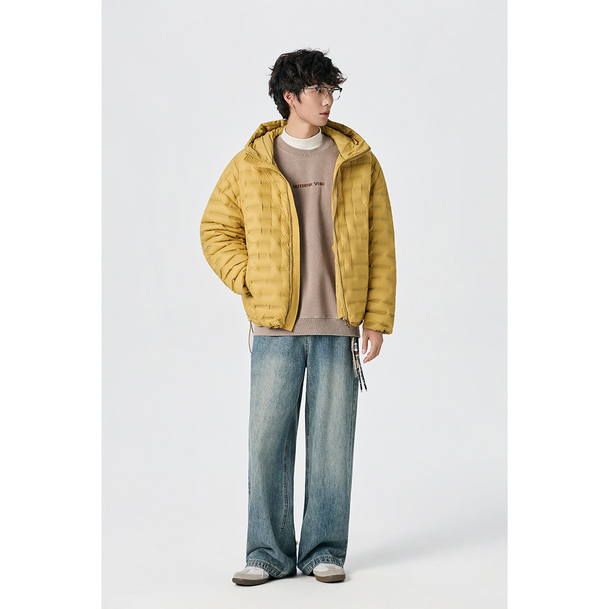Model wearing a mustard-yellow hooded quilted jacket with a sweatshirt and loose blue jeans.