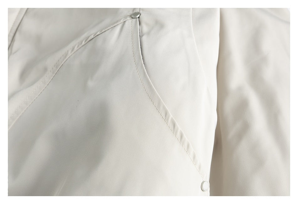Close-up of an ivory coat showing a curved seam and two round snap fasteners.
