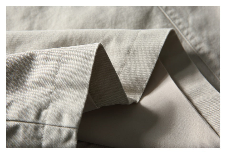 Close-up of light beige woven fabric draped in angular folds, showing its fine textured surface.