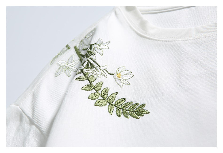 Close-up of a white shirt with green leafy and white flower embroidery near the shoulder.