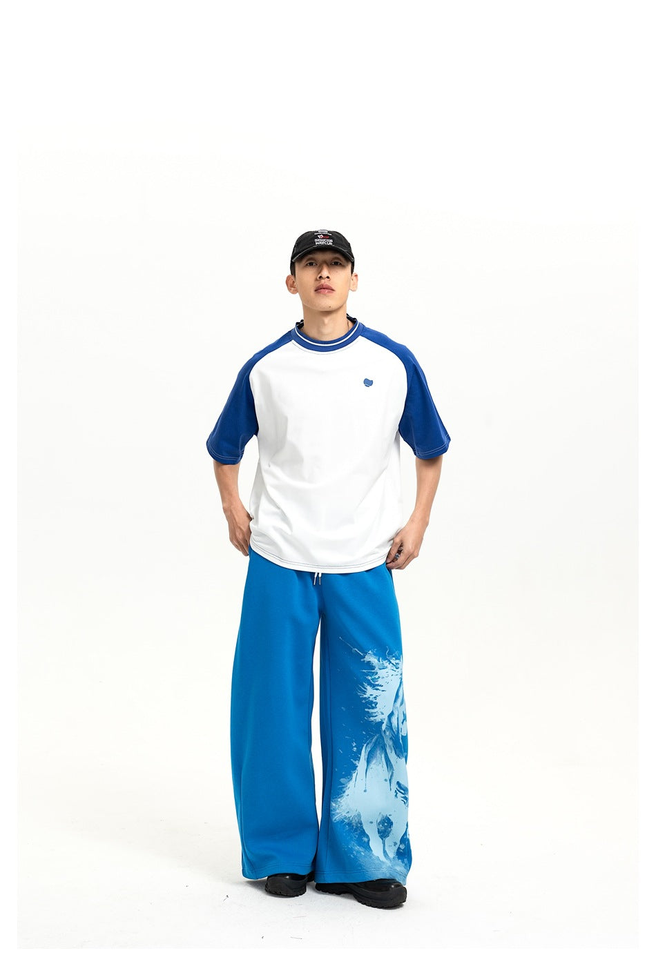 Full-length front view of a model in a white T-shirt with blue raglan sleeves and blue wide-leg pants with a horse graphic.