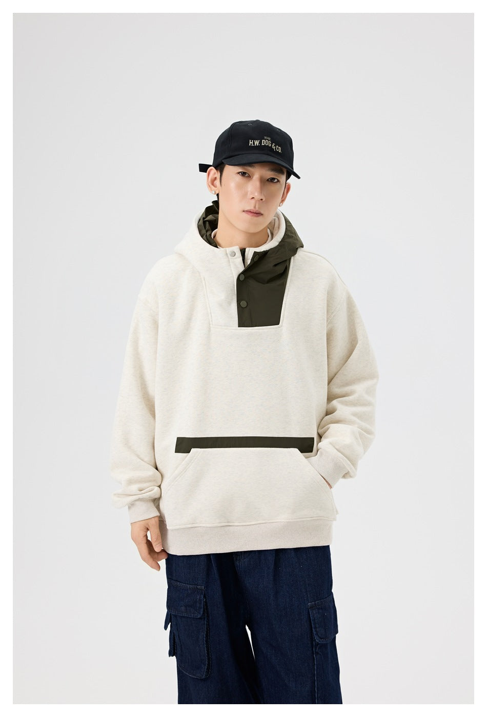 Close front view of a model wearing an ivory hoodie with an olive hood panel, snap placket and kangaroo pocket.