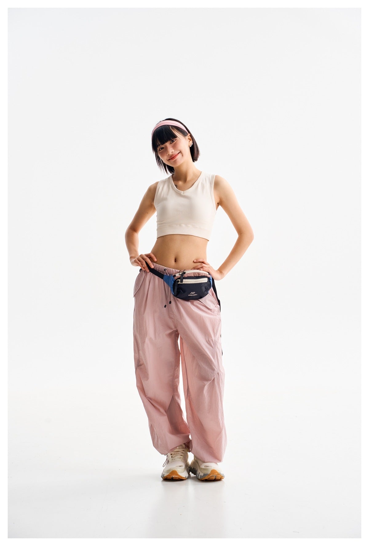 Front view of a model wearing loose light pink drawstring pants and a white crop top.