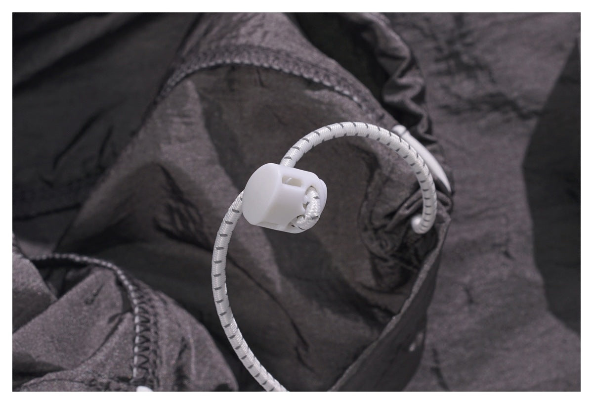 Close-up of a white cord and toggle drawstring against dark charcoal fabric.