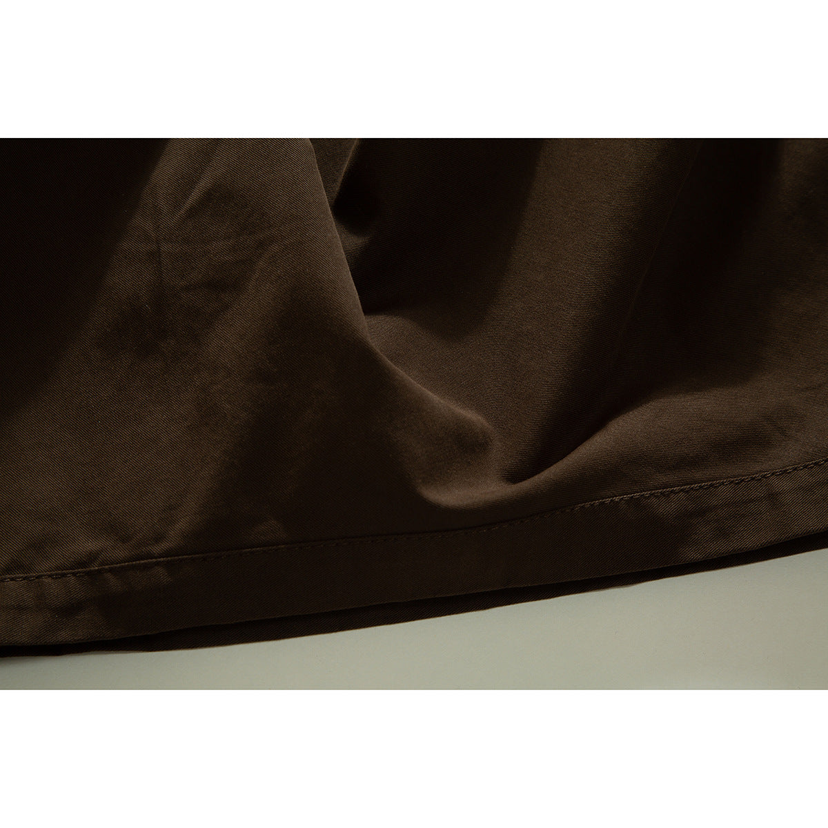 Close-up of the brown skirt's stitched lower hem and softly draped fabric.