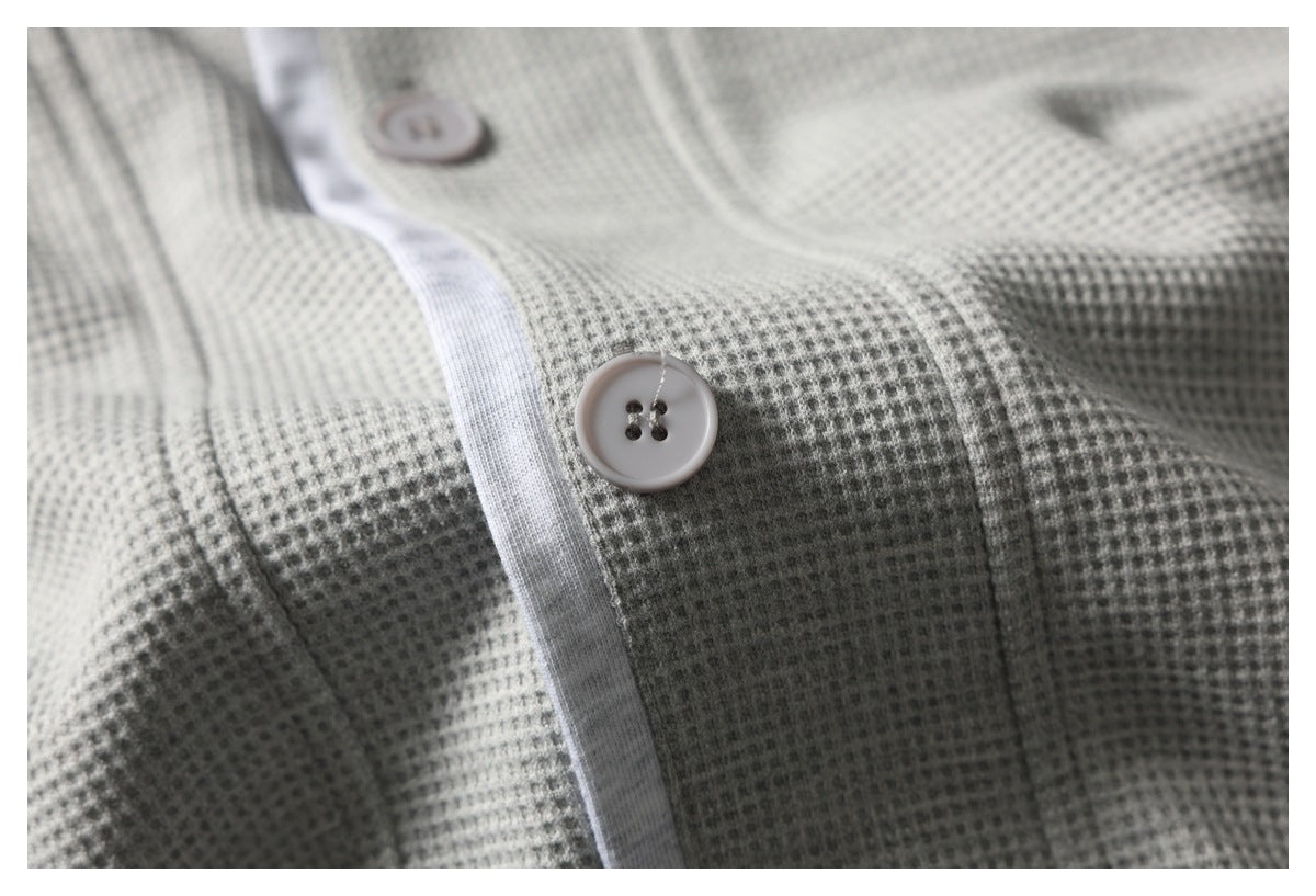 Close-up of a pale button and placket against the top's light gray textured fabric.