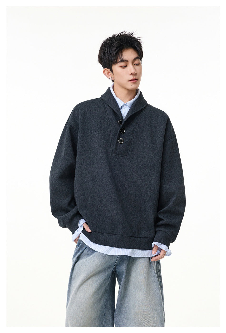 Front view of a model wearing a charcoal oversized pullover with a shawl collar and three-button placket over a pale blue