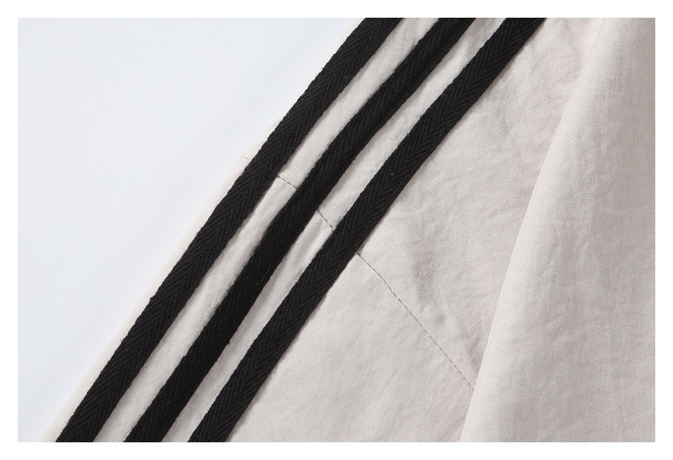 Close-up of three raised black stripes running along the off-white shirt's shoulder and sleeve.