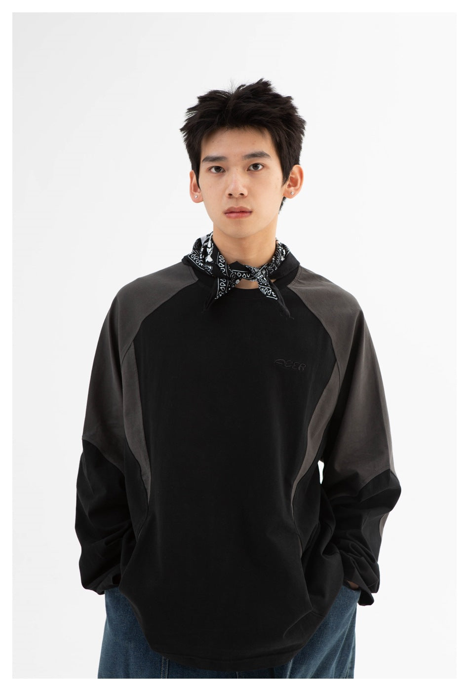 Close front view of a model wearing a black sweatshirt with charcoal shoulder panels and a patterned neck scarf.