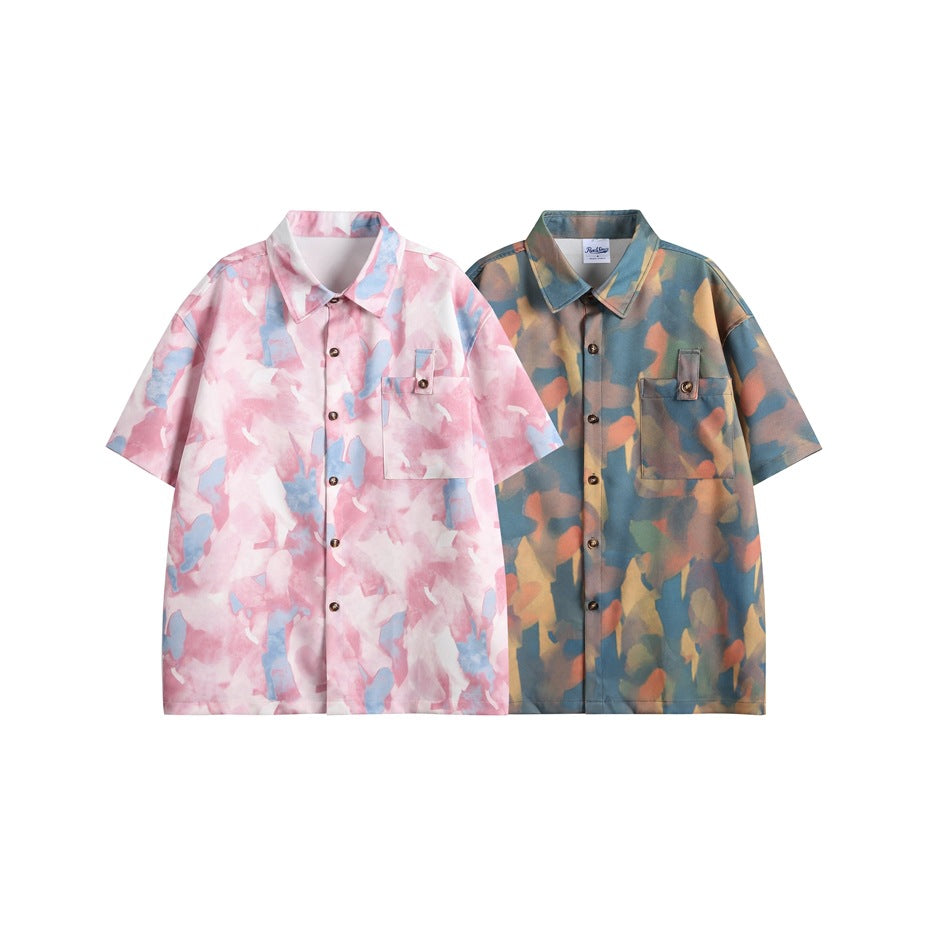 Two short-sleeve button-up shirts shown side by side: one pink and blue abstract print, one dark blue with warm-toned print.
