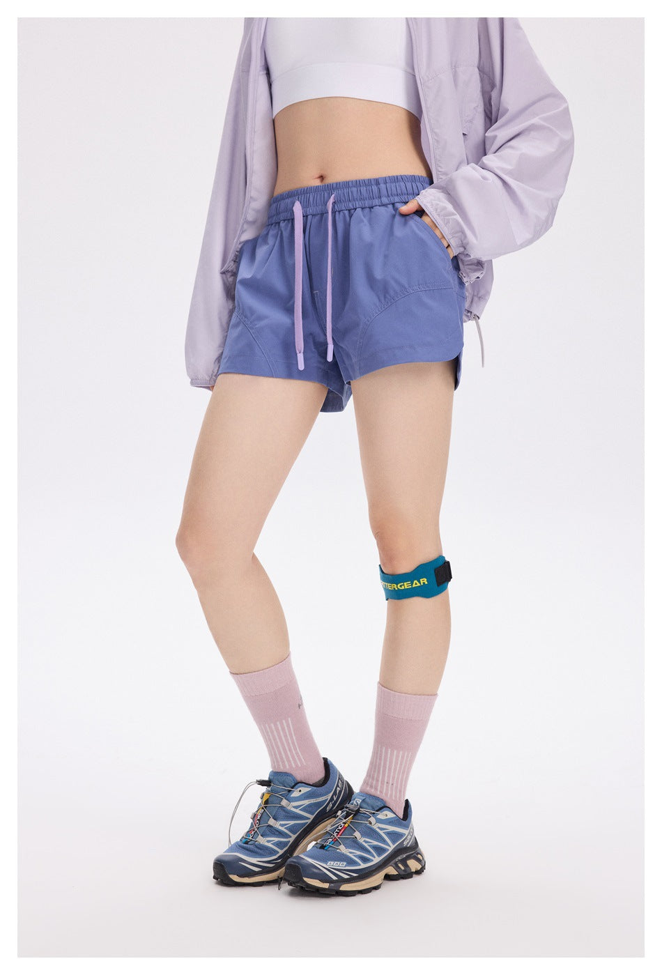 Angled front view of a model wearing blue-violet running shorts with a lilac drawstring and curved pockets.