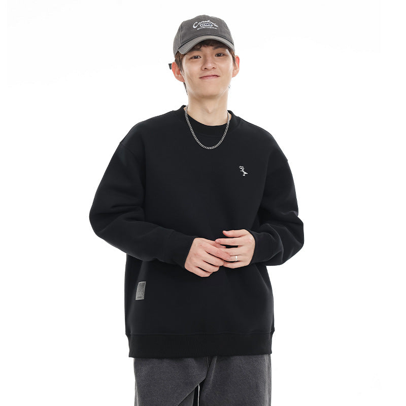 Model wearing a black crewneck sweatshirt with a small chest embroidery and a rectangular hem patch.