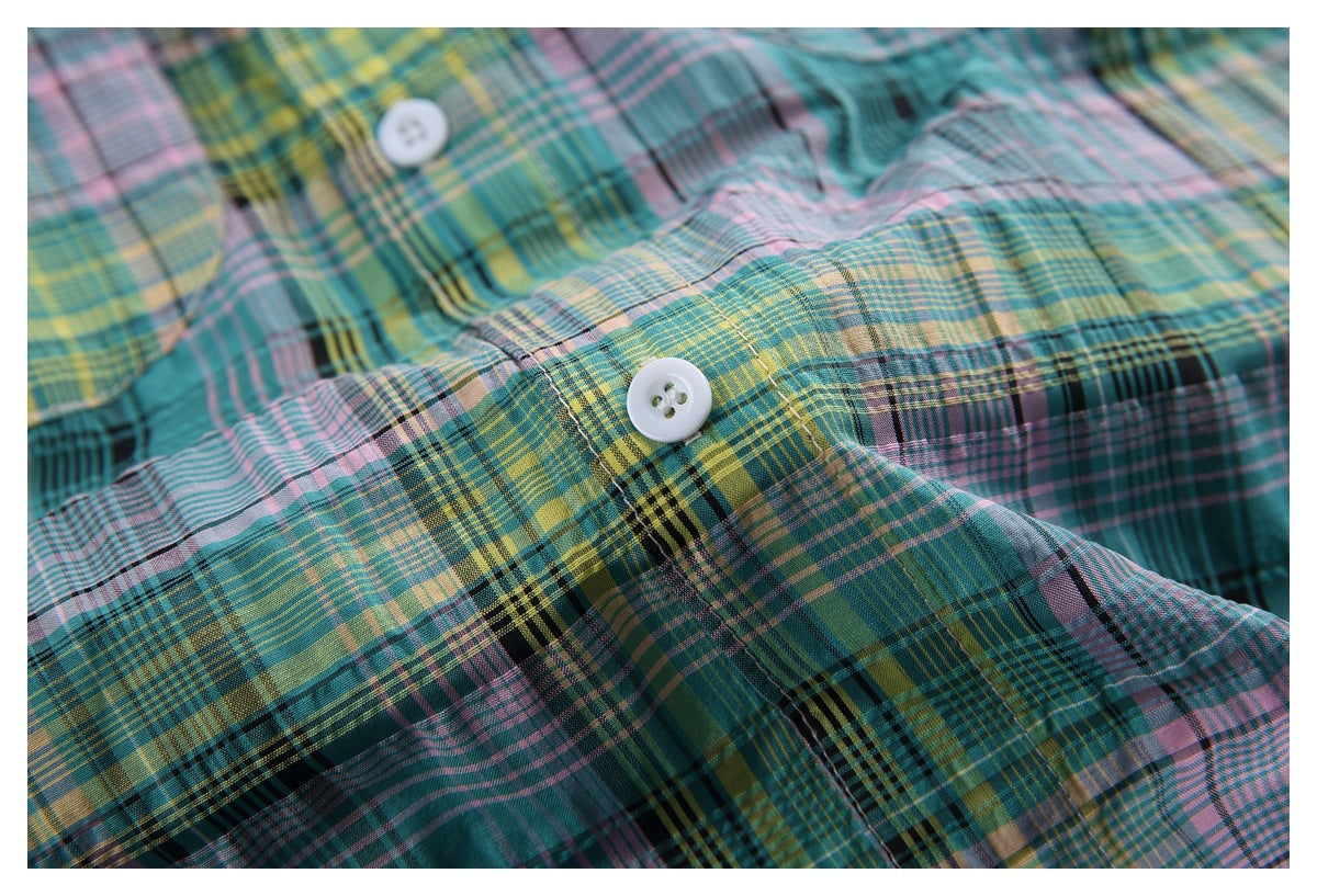 Close-up of a white button on a teal, pink, yellow, and black plaid shirt.