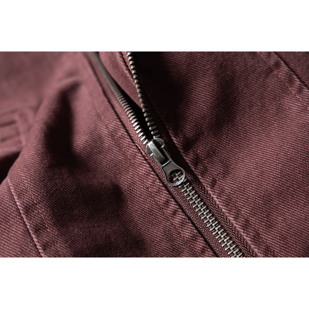 Close-up of a dark metal zipper and burgundy fabric on a jacket.