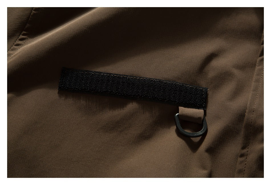 Close-up of a dark brown jacket with a black hook-and-loop tab and small D-ring.