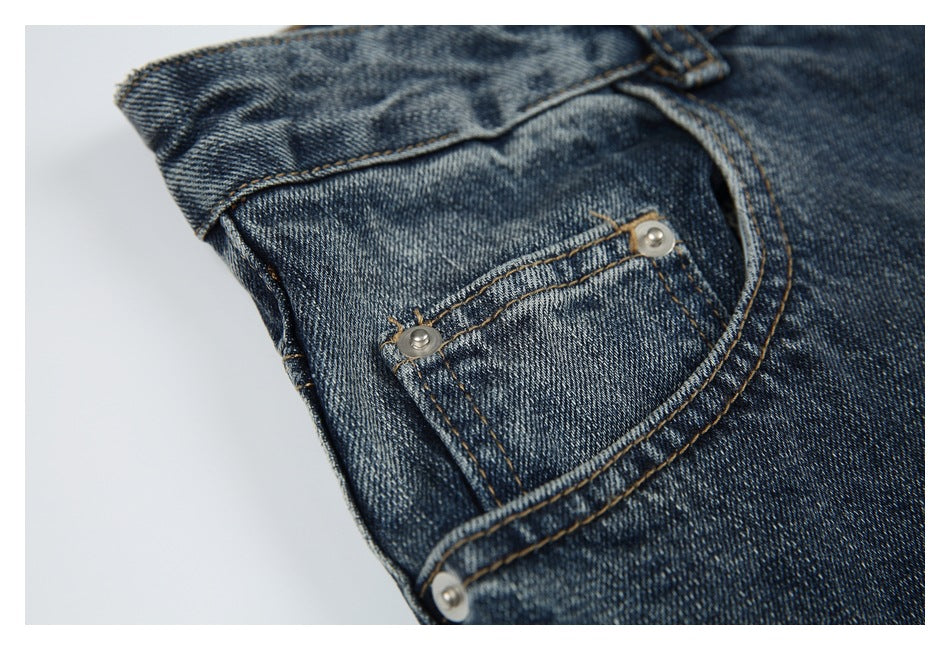 Close-up of a small riveted pocket and curved seam on dark blue jeans.