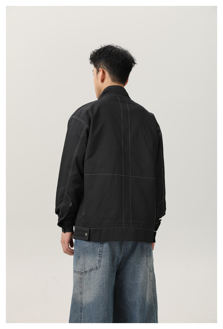 Back view of a model in a black jacket with contrast stitching and a high collar.