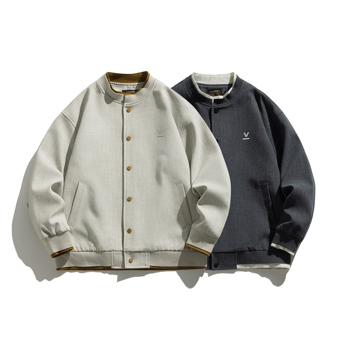 Front view of two snap-front jackets in light beige and charcoal, with stand collars, pockets, and ribbed cuffs and hems.