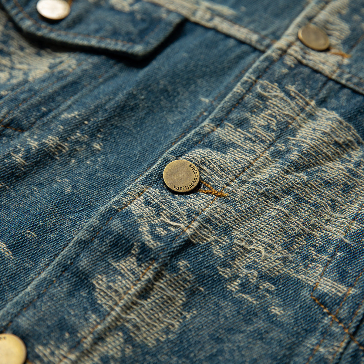 Close-up of distressed blue denim with a brass-tone button engraved with a small brand name.