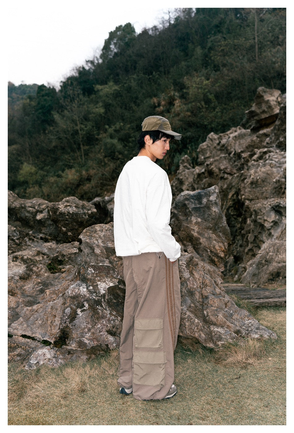 Rear three-quarter view of a model wearing a white long-sleeve shirt and taupe cargo pants with side stripes.