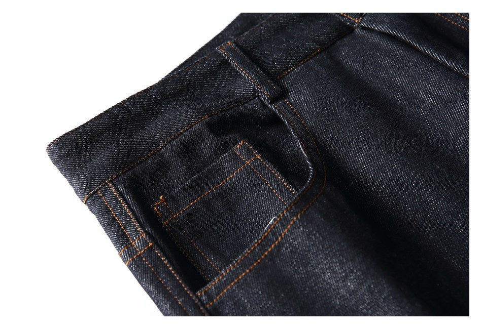Close-up of a small pocket and belt loop on dark indigo jeans, finished with orange stitching.
