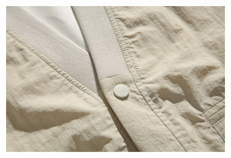 Close-up of the beige jacket's ribbed trim, stitched front placket, and round white button.