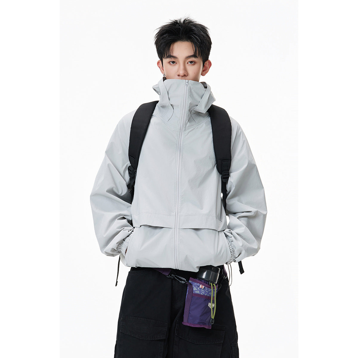 Waist-up view of a model wearing a light gray high-collar zip jacket with a backpack.