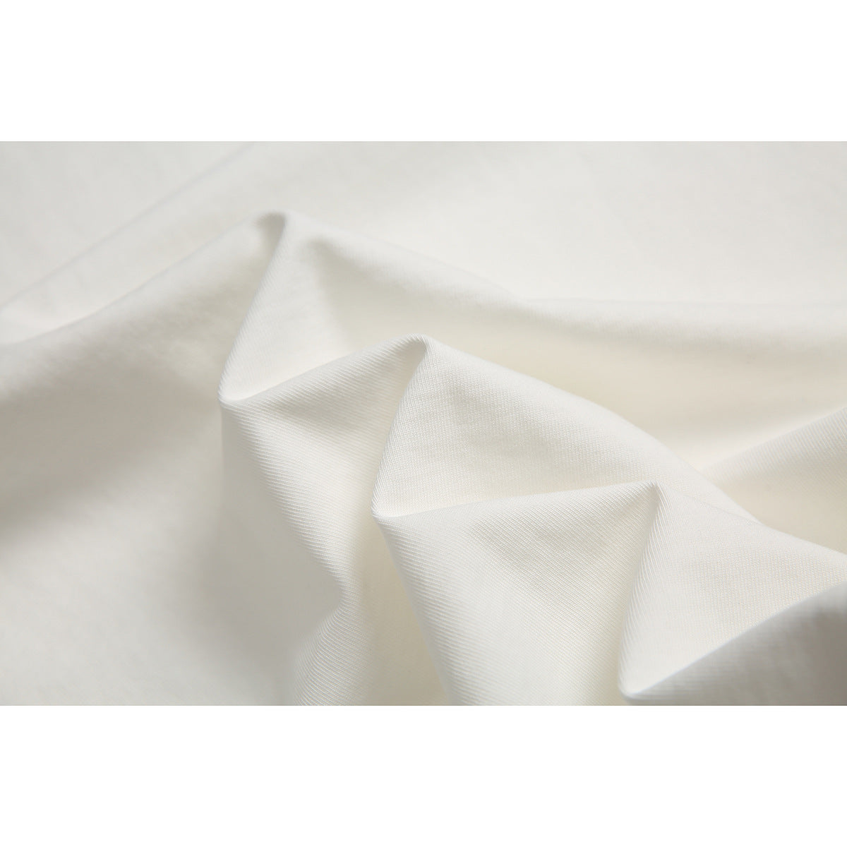 Close-up of off-white garment fabric draped into soft folds, showing its fine surface texture.