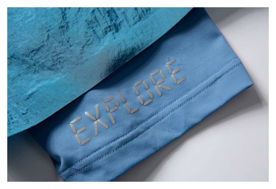 Close-up of a blue garment hem with gray “EXPLORE” lettering and visible double stitching.