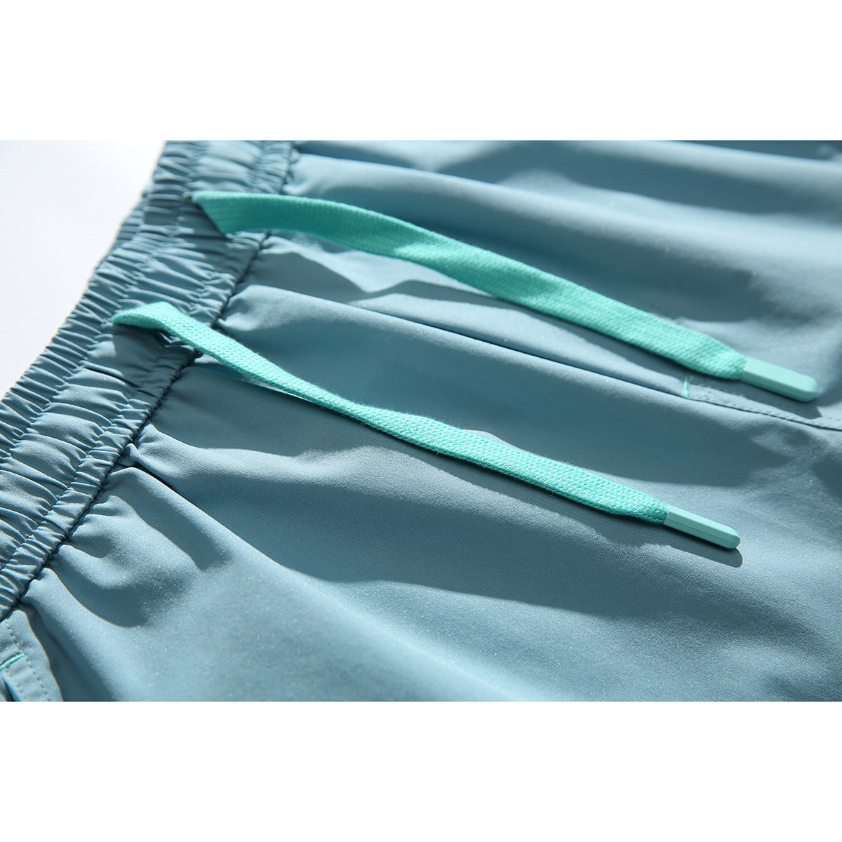 Close-up of light blue shorts with an elastic waistband and two turquoise drawstrings.