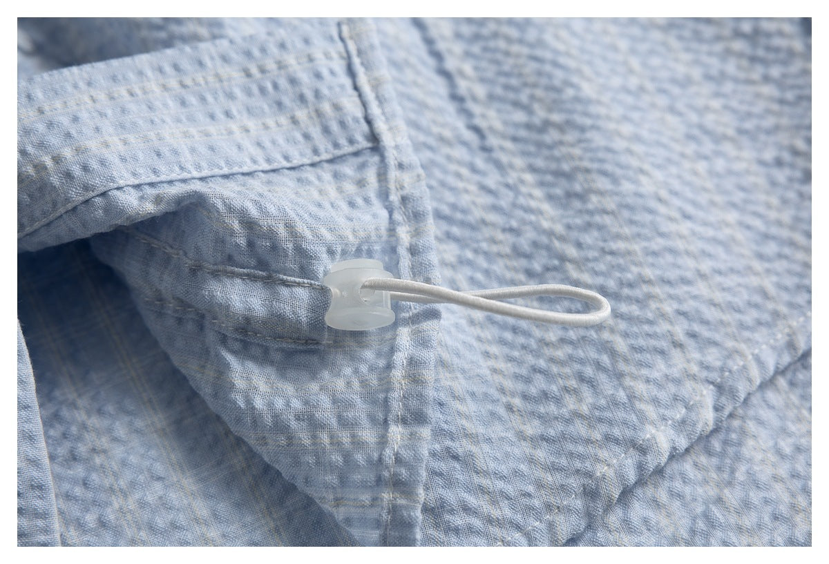 Close-up of a white elastic loop and plastic toggle on light blue-gray textured fabric.