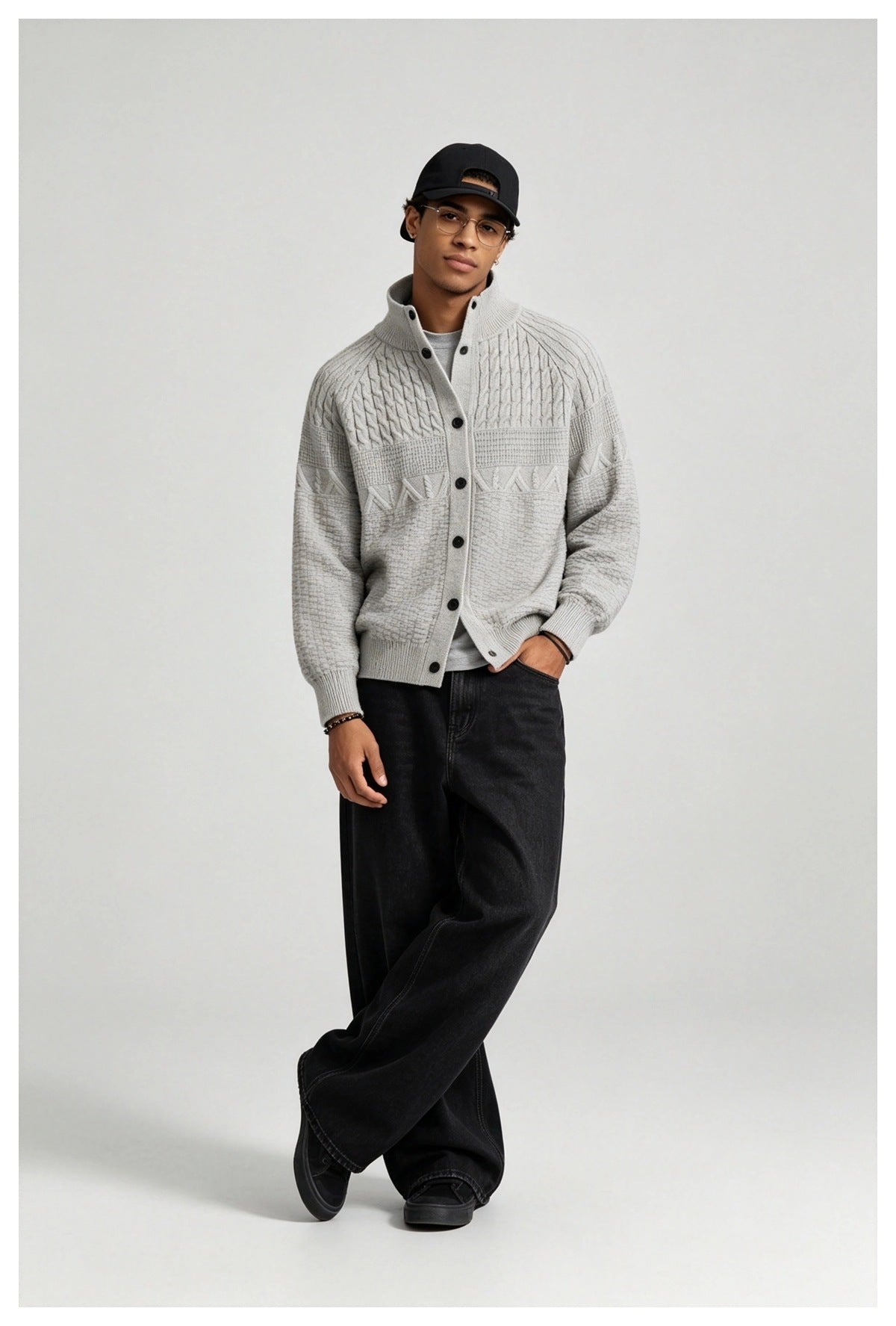 Man wearing the light gray textured knit button cardigan over a gray tee with black wide-leg jeans and a black cap