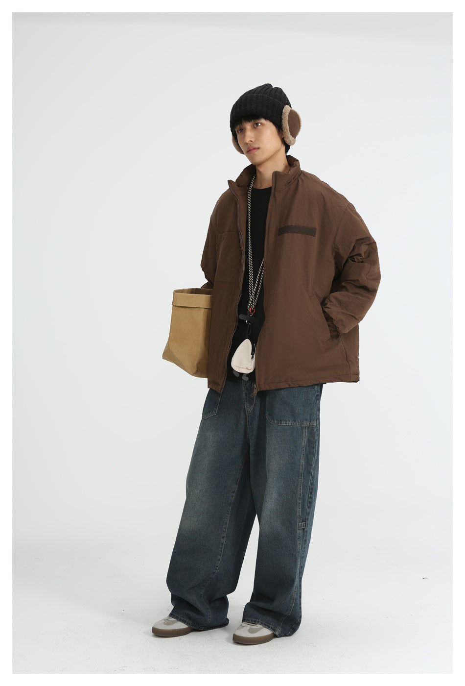 Model wearing brown zip jacket with hand in pocket, beanie and wide-leg jeans, three-quarter view