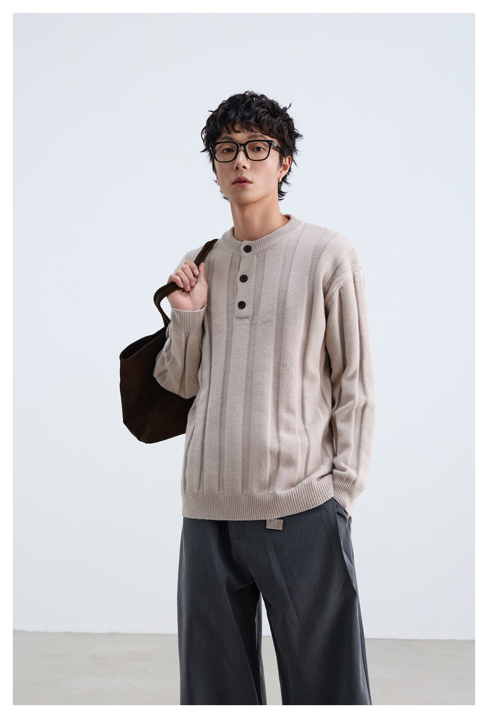 Model wearing a pale beige sweater with vertical ribbed panels and a three-button neck, paired with dark trousers.
