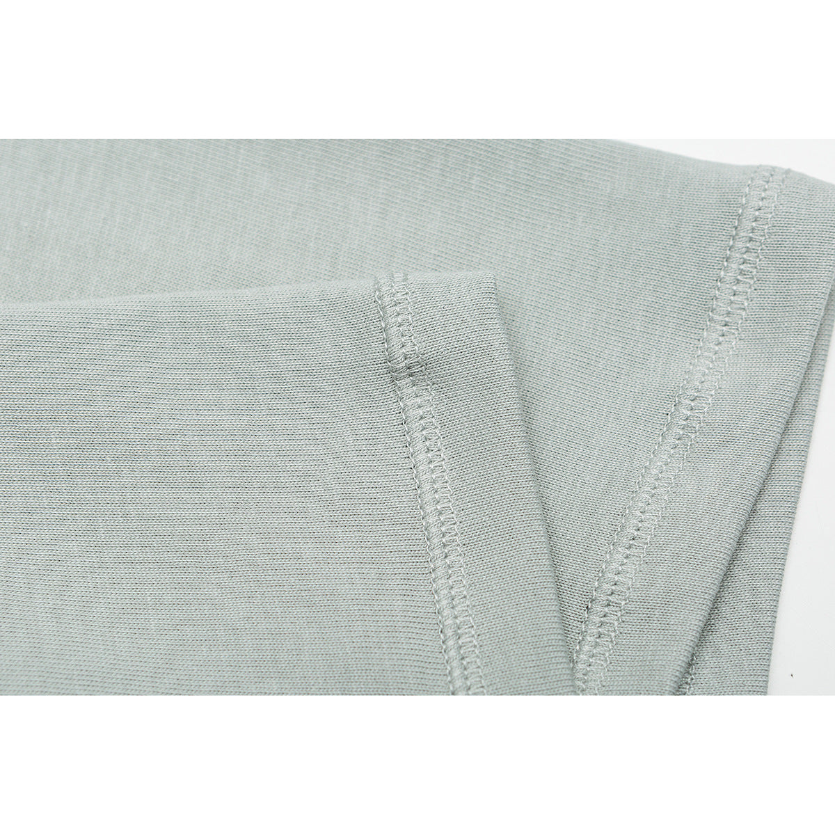 Close-up of pale sage shirt fabric showing overlocked seams and a folded edge.
