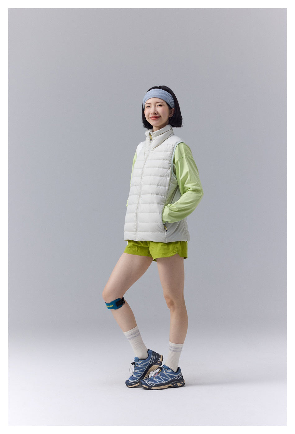 Woman wearing a white quilted zip vest over a light green top and lime shorts, standing at a slight angle.