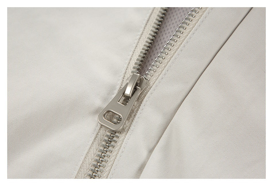 Close-up of the off-white jacket's metal zipper and pull between stitched fabric panels.