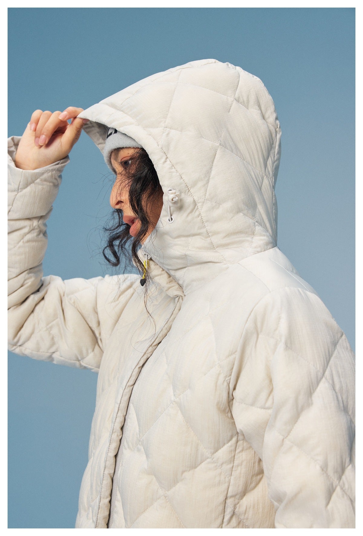 Side close-up of the cream quilted coat's hood, adjustable drawcord toggle and diamond stitching.