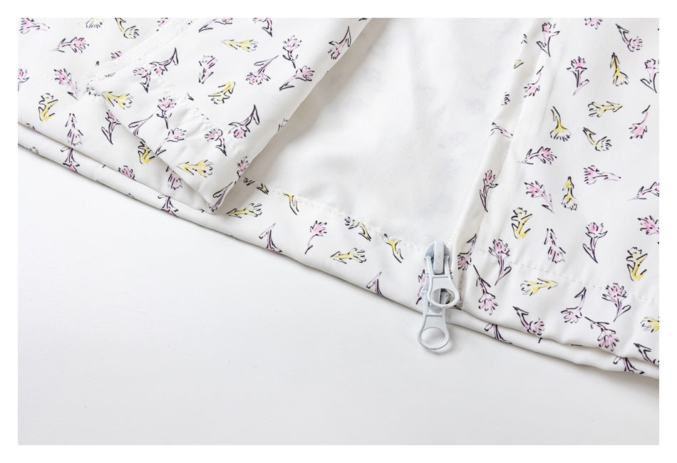 Close-up of a white garment with pink and yellow floral print, showing a zipper and pull tab along a seam.