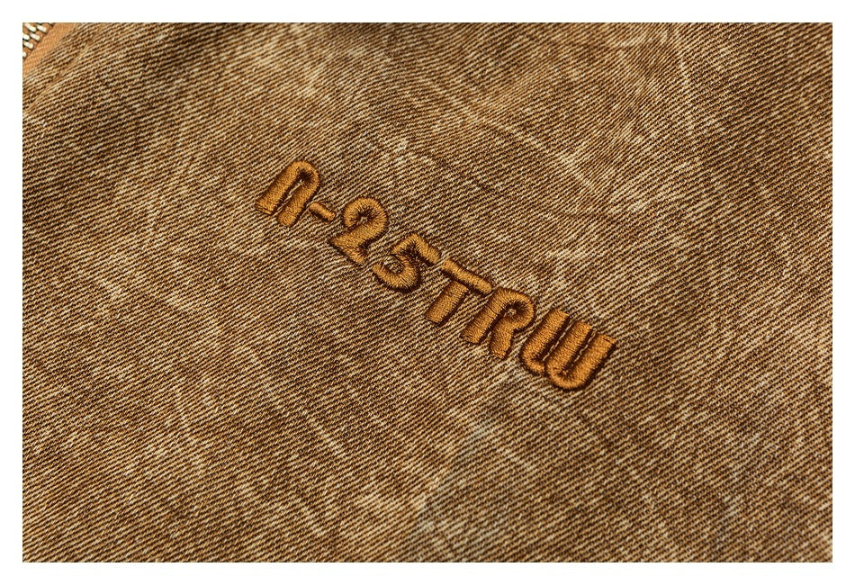 Close-up of embroidered lettering on the mottled tan jacket fabric.
