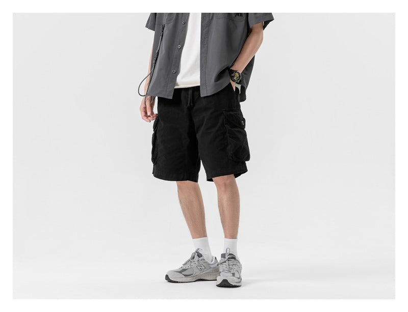 Model wearing black cargo shorts with large flap pockets, shown from the front in a relaxed stance.