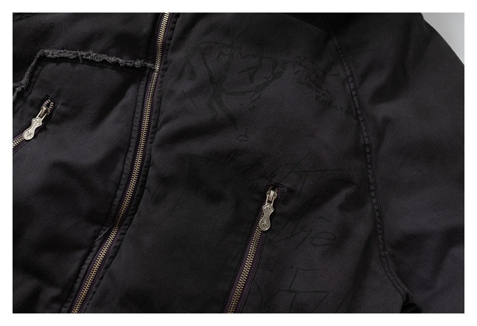 Black jacket close-up with two zip pockets, frayed trim, and a subtle dark graphic on the fabric.
